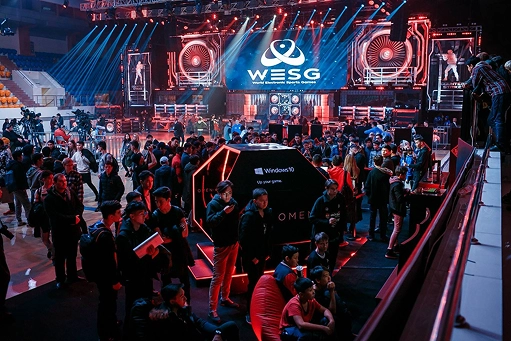 Grote e-sportevenementhal met publiek, podiumverlichting en het WESG-toernooischerm op de achtergrond.